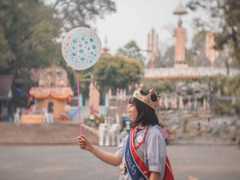 Side view of young woman holding balloon while standing on road