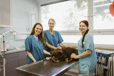 Portrait of smiling nurses and female veterinarian with bulldog on table in medical clinic