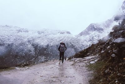 Rear view of woman standing on snowcapped mountain against sky