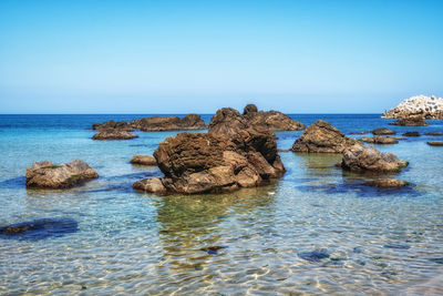 Rocks in sea against clear blue sky