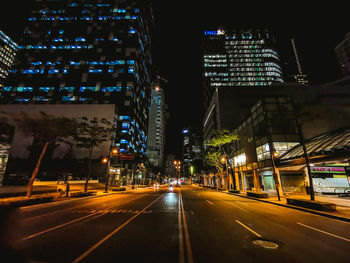 Illuminated street by buildings in city at night