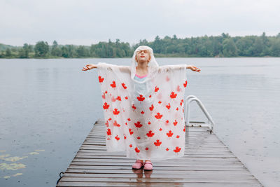 Girl wearing raincoat standing on pier with arms outstretched