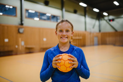 Portrait of smiling girl holding handball in sports court