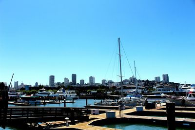 Sailboats moored in harbor against clear blue sky