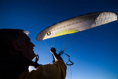 Low angle view of man flying against clear blue sky