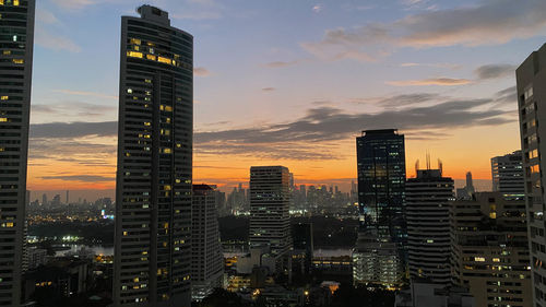 Illuminated buildings in city against sky at sunset