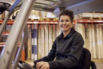 Portrait of smiling female operator driving forklift in lumber industry