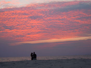 Couple standing at beach against sky during sunset