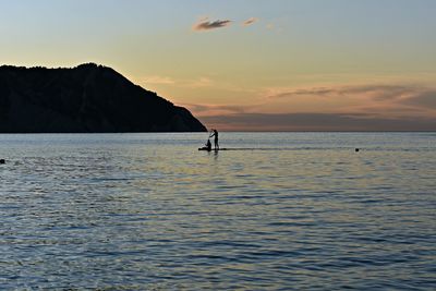 Silhouette person in sea against sky during sunset