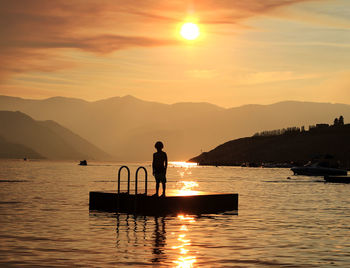 Silhouette boy standing on floating platform in lake