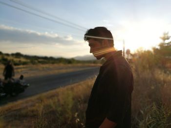 Side view of man standing on field against sky