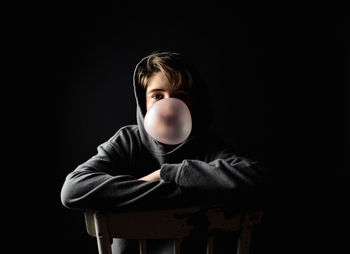 Portrait of cute boy sitting against black background