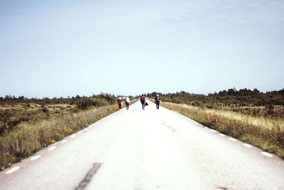 Rear view of people walking on road along landscape