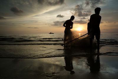 Silhouette people standing on beach against sky during sunset