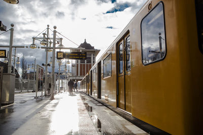 Yellow train at wet railroad station against cloudy sky during sunny day