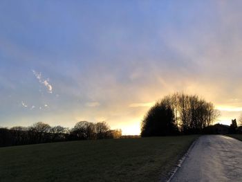 Road amidst trees against sky during sunset