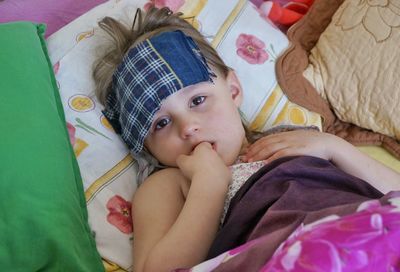 Portrait of cute girl with fever lying on bed