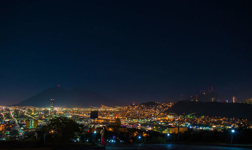 Illuminated cityscape against clear blue sky at night