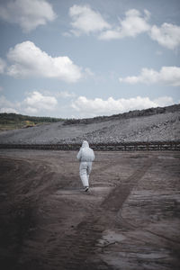 Rear view of worker in protective clothing walking on field at mining industry against sky
