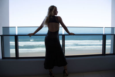 Rear view of woman standing by swimming pool against sky