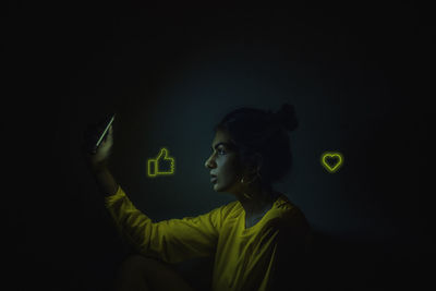 Profile view of woman using phone with icons in darkroom