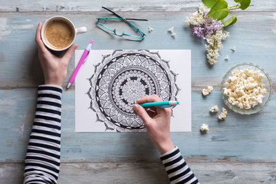 Cropped hand of woman drawing in paper at table