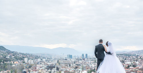 Rear view of couple kissing against sky in city