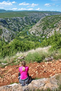 Rear view of female hiker looking at view while sitting at mountain