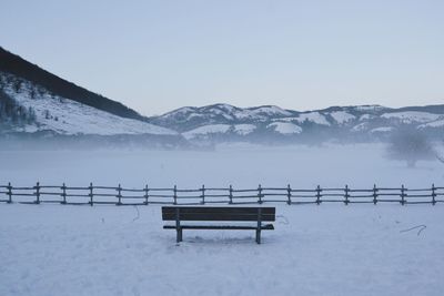 Bench in snow covered mountains against sky