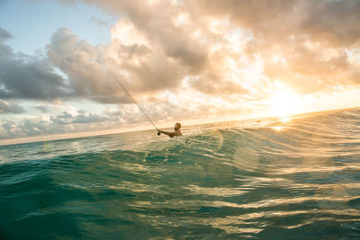 Shirtless man fishing in sea against sky during sunset