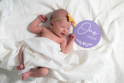 Portrait of cute baby girl sleeping on bed at home next to a one week old sign