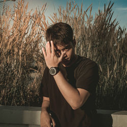 Young man looking away while standing against plants