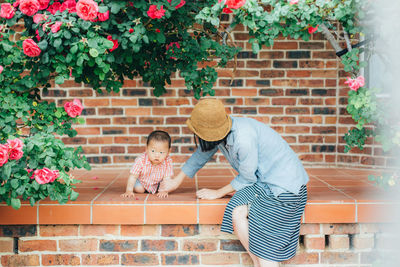 Mother with holding son while sitting against brick wall