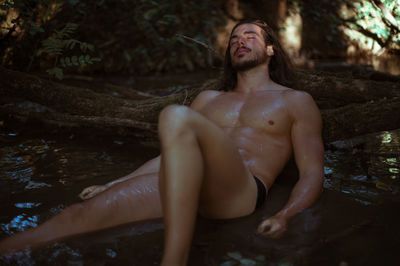 Shirtless young man sleeping by log in lake