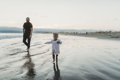 Young toddler girl running on the beach with dad in ocean
