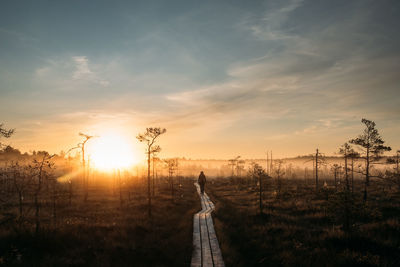 Woman standing on field against sky during sunset