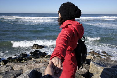 Cropped image of man holding woman hand at beach against sky