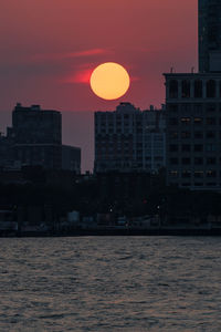 Buildings by sea against sky during sunset
