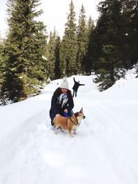 Woman with dog on snowy field against trees