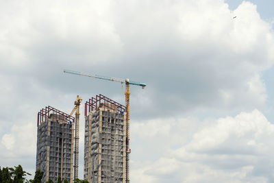 Low angle view of crane by building against sky