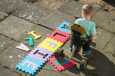 High angle view of boy riding tricycle by text on footpath