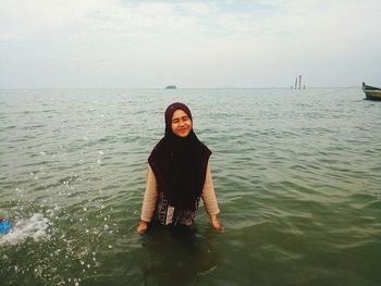 Portrait of smiling young woman standing in sea against sky