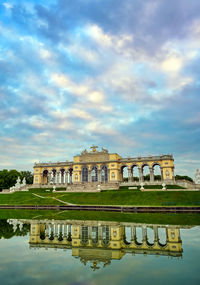 Reflection of building in lake against cloudy sky