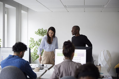 Man and woman talking inn office while other coworkers using computers