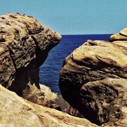 Rock formations by sea against clear sky