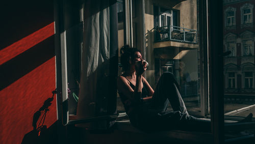 Full length of woman sitting by window in darkroom