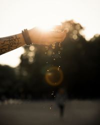 Close-up of water drops on hand against sky during sunset