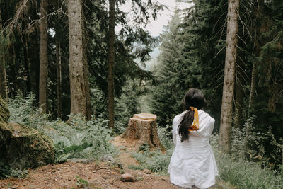 Rear view of woman standing amidst trees in forest