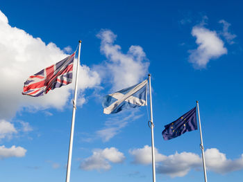 Low angle view of british, scottish and european flags against blue sky