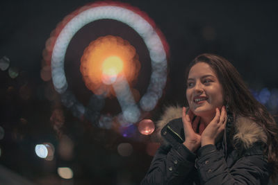 Cheerful young woman standing against illuminated ferris wheel at night